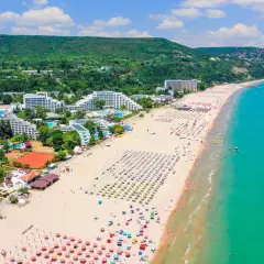 Słoneczne bułgarskie plaże tętnią życiem. Widać hotele, baseny, korty tenisowe i mnóstwo kolorowych parasoli na piaszczystym brzegu.