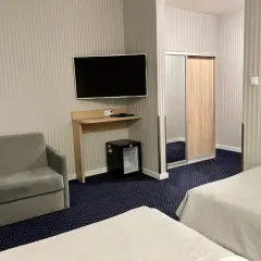 Pokój w sanatorium Arka Kołobrzeg: dwa łóżka, sofa, szafa z lustrem, telewizor i mini lodówka.
