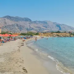 Słoneczna plaża w Frangokastello z turkusową wodą, leżakami i widokiem na zabytkowy zamek.