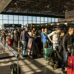 Kolejka pasażerów z bagażami na lotnisku we Włoszech. W tle widać stanowiska odprawy.