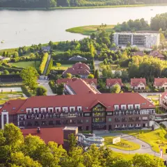 Widok na kompleks wypoczynkowy z hotelem Radisson, basenami i jeziorem. Widać też domy i las.