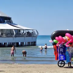 Słoneczna durres plaża z wózkiem pełnym dmuchanych zabawek i restauracją na wodzie.