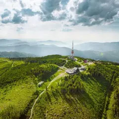 Widok z lotu ptaka na zielone, zalesione **beskidy szczyty** z wieżą telekomunikacyjną i budynkami na jednym ze wzniesień.