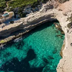 Malta plaże: turkusowa woda, skaliste wybrzeże i mały domek na klifie. Dwie osoby spacerują ścieżką.