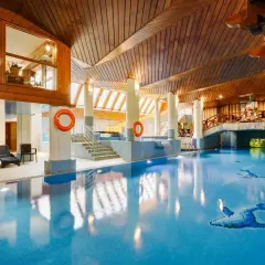 Basen w hotelu Belvedere Resort & Spa z drewnianym sufitem i mostkiem. Woda jest błękitna, a na dnie widać mozaiki z ptakami.