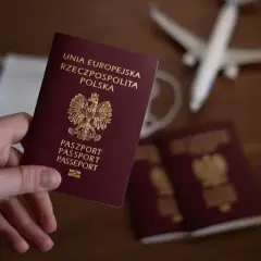Dłoń trzyma polski paszport. Obok leżą kolejne paszporty, maseczka i samolot. Czas na podróż, ale ile wyrabia się paszport?