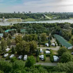 Malta hotel camping: kampery i przyczepy kempingowe wśród zieleni, z widokiem na jezioro i miasto w tle.
