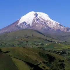 Pokryty śniegiem wulkan Chimborazo, uznawany za największą górę na świecie od środka Ziemi, góruje nad zielonymi, pofałdowanymi wzgórzami i polami.