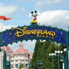 Brama do Disneyland Paris z Myszka Miki na szczycie. W tle różowe budynki i zielone drzewa.