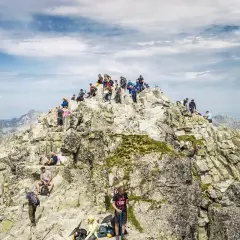 Tłum turystów na skalistym szczycie, najwyższy szczyt w Polsce, podziwia panoramę Tatr.