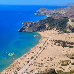 Malownicza grecja plaża z turkusową wodą, piaszczystym brzegiem pełnym leżaków i wodnym parkiem rozrywki.