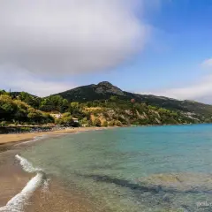 Piękna plaża Tragaki Zakynthos z turkusową wodą, zielonymi wzgórzami i rzędem leżaków pod parasolami.
