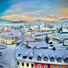 Zimowy krajobraz miasta w Czechach blisko granicy. Śnieg pokrywa dachy i ulice, a w oddali widać mgliste wzgórza.