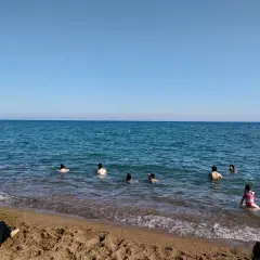 Słoneczny dzień na plaży Lara. Ludzie kąpią się w turkusowym morzu, a na piasku odpoczywają inni plażowicze.