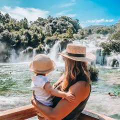Mama z dzieckiem podziwia piękne wodospady Krka. Woda w rzece jest krystalicznie czysta, a wokół bujna zieleń.