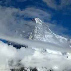 Majestatyczny, ośnieżony szczyt K2, najwyższy szczyt Karakorum, wyłania się z chmur na tle błękitnego nieba.