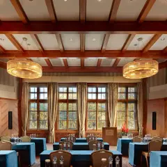 Elegancka sala konferencyjna w Kempinski Hotel, z drewnianymi belkami na suficie, dużymi oknami z widokiem na jesienny krajobraz i stylowymi żyrandolami.