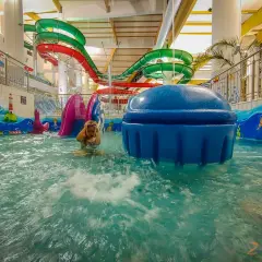 Dziecko bawi się w wodzie w aquaparku hotelu Crocus, w tle kolorowe zjeżdżalnie.