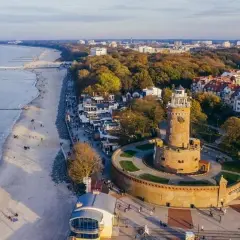 Widok na latarnie morskie w Polsce, z charakterystyczną wieżą w Kołobrzegu, plażą i morzem.