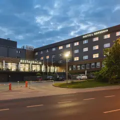 Hotel Kopernik Olsztyn z neonowym napisem "RESTAURACJA" i oświetlonymi oknami. Zapraszamy na nocleg i pyszne jedzenie.