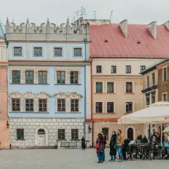 Kolorowe kamienice na rynku, idealne na tani city break. Ludzie spacerują, siedzą w ogródku kawiarnianym.