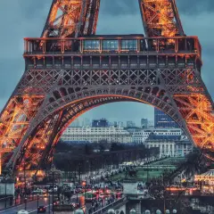 Eiffel rozświetlona pomarańczowym blaskiem, z widokiem na paryskie ulice i budynki.