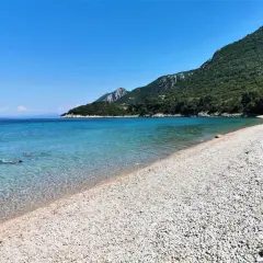 Chorwacja plaże piaszczyste, krystalicznie czysta woda i zielone wzgórza. Dwie osoby pływają w morzu.
