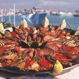 Bogata paella z owocami morza, rybą i warzywami, ozdobiona cytryną. Prawdziwy smak kuchni hiszpańskiej nad brzegiem morza.