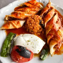 Pyszne tureckie jedzenie: rolady z mięsem w sosie pomidorowym, ryż bulgur, pieczona papryka i pomidor, oraz biały ser.