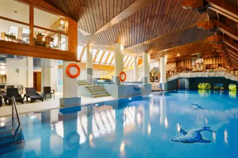 Basen w hotelu Belvedere Resort & Spa z drewnianym sufitem i mostkiem. Woda jest błękitna, a na dnie widać mozaiki z ptakami.