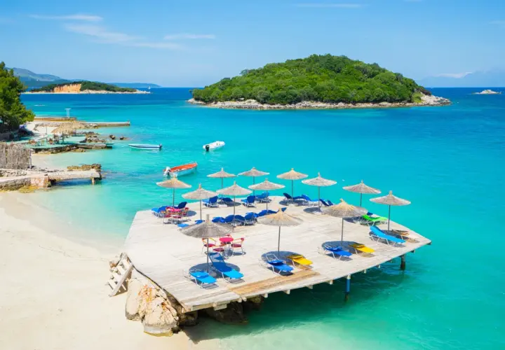 Rajskie albania plaże z turkusową wodą, drewnianym molo i leżakami pod parasolami.