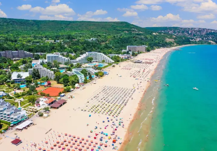 Słoneczne bułgarskie plaże tętnią życiem. Widać hotele, baseny, korty tenisowe i mnóstwo kolorowych parasoli na piaszczystym brzegu.