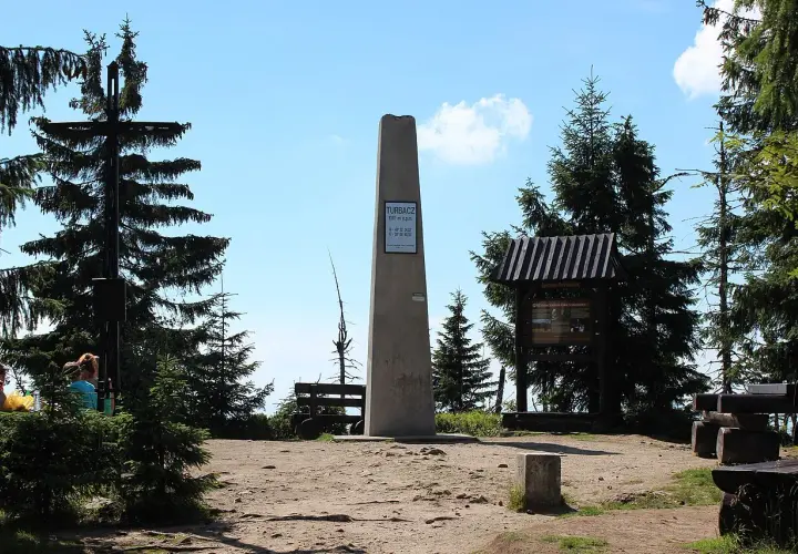 Szczyt Turbacz, 1310 m n.p.m. – ile się idzie? Widok na obelisk, krzyż i tablice informacyjne w otoczeniu górskich lasów.