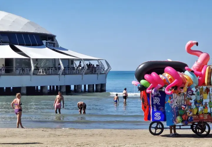 Słoneczna durres plaża z wózkiem pełnym dmuchanych zabawek i restauracją na wodzie.