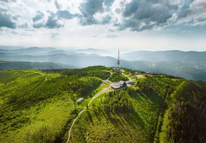 Widok z lotu ptaka na zielone, zalesione **beskidy szczyty** z wieżą telekomunikacyjną i budynkami na jednym ze wzniesień.