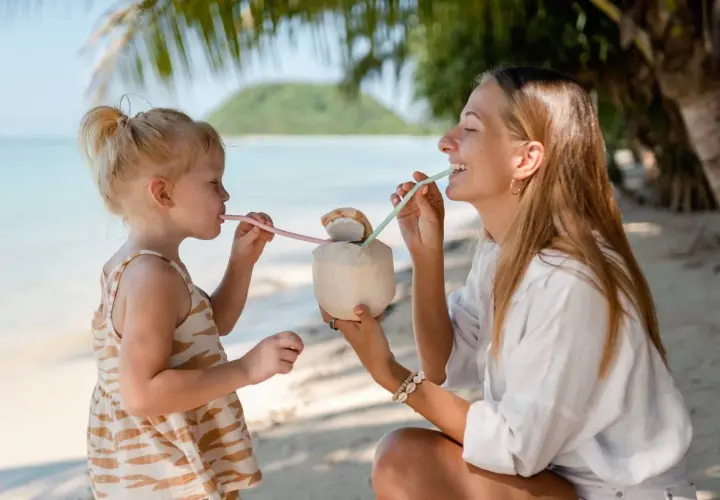 Mama i córka piją kokosa na plaży w Sanur. Słoneczny dzień, palmy i ocean tworzą rajski widok.