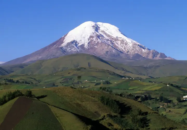 Pokryty śniegiem wulkan Chimborazo, uznawany za największą górę na świecie od środka Ziemi, góruje nad zielonymi, pofałdowanymi wzgórzami i polami.