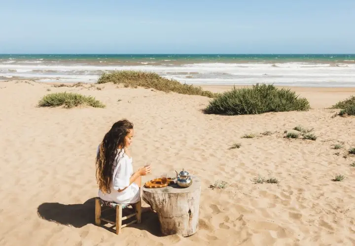 Kobieta pije herbatę na piaszczystej plaży w Tunezji, z widokiem na ocean.