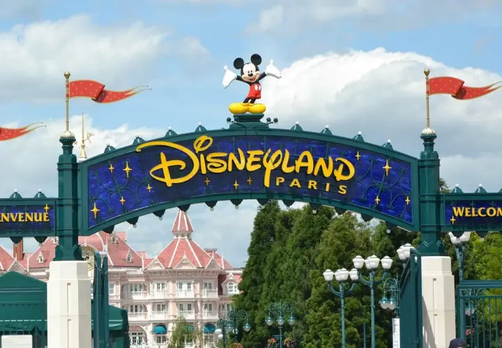Brama do Disneyland Paris z Myszka Miki na szczycie. W tle różowe budynki i zielone drzewa.