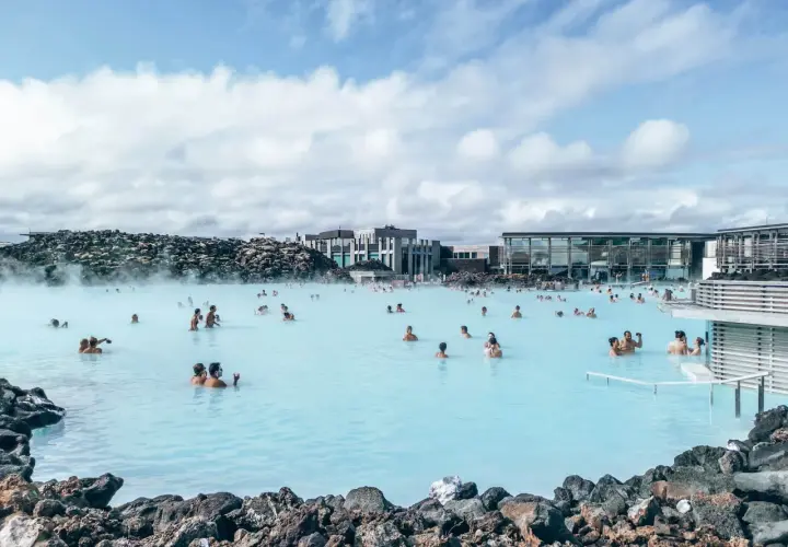 Ludzie kąpią się w turkusowej wodzie geotermalnego **blue lagoon** otoczonej wulkanicznymi skałami.