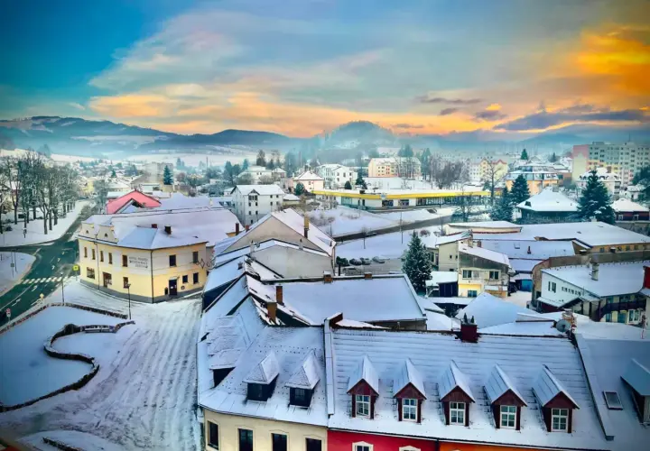 Zimowy krajobraz miasta w Czechach blisko granicy. Śnieg pokrywa dachy i ulice, a w oddali widać mgliste wzgórza.