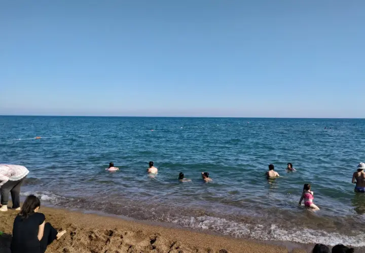 Słoneczny dzień na plaży Lara. Ludzie kąpią się w turkusowym morzu, a na piasku odpoczywają inni plażowicze.