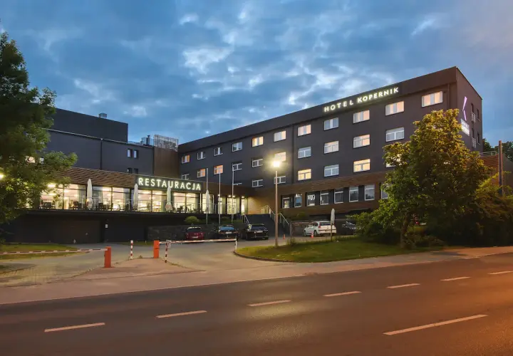 Hotel Kopernik Olsztyn z neonowym napisem "RESTAURACJA" i oświetlonymi oknami. Zapraszamy na nocleg i pyszne jedzenie.