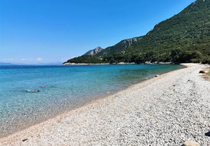 Chorwacja plaże piaszczyste, krystalicznie czysta woda i zielone wzgórza. Dwie osoby pływają w morzu.