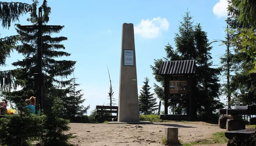 Szczyt Turbacz, 1310 m n.p.m. – ile się idzie? Widok na obelisk, krzyż i tablice informacyjne w otoczeniu górskich lasów.