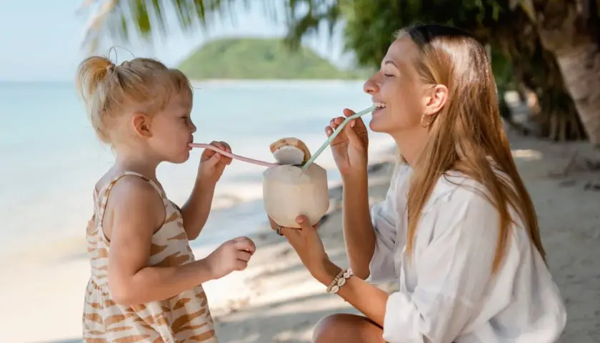 Mama i córka piją kokosa na plaży w Sanur. Słoneczny dzień, palmy i ocean tworzą rajski widok.