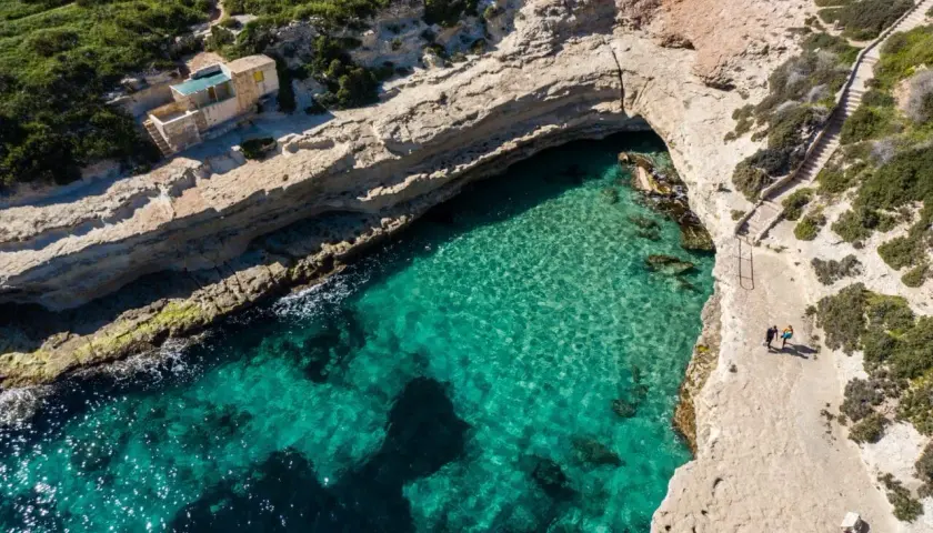 Malta plaże: turkusowa woda, skaliste wybrzeże i mały domek na klifie. Dwie osoby spacerują ścieżką.