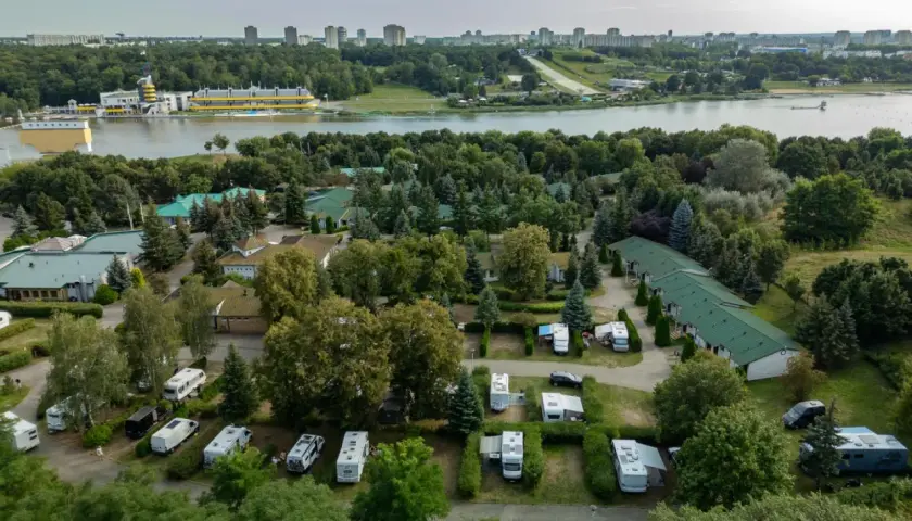 Malta hotel camping: kampery i przyczepy kempingowe wśród zieleni, z widokiem na jezioro i miasto w tle.