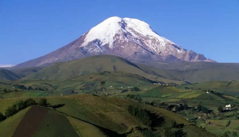 Pokryty śniegiem wulkan Chimborazo, uznawany za największą górę na świecie od środka Ziemi, góruje nad zielonymi, pofałdowanymi wzgórzami i polami.