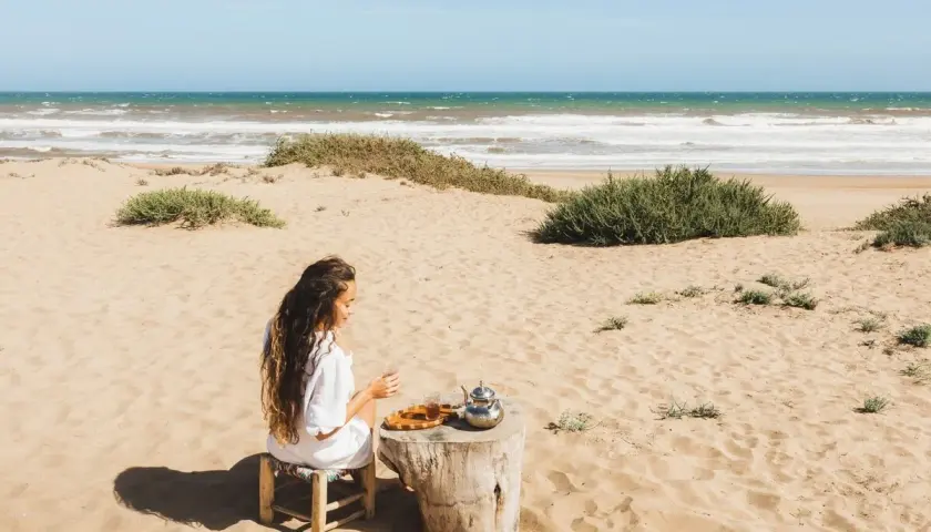 Kobieta pije herbatę na piaszczystej plaży w Tunezji, z widokiem na ocean.